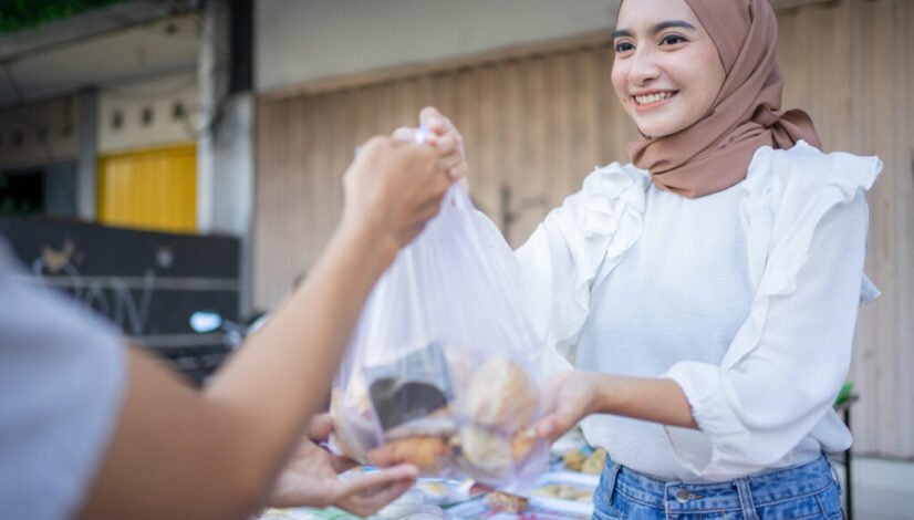 An asian girl in a veil gives takjil food orders in plastic bags to buyer