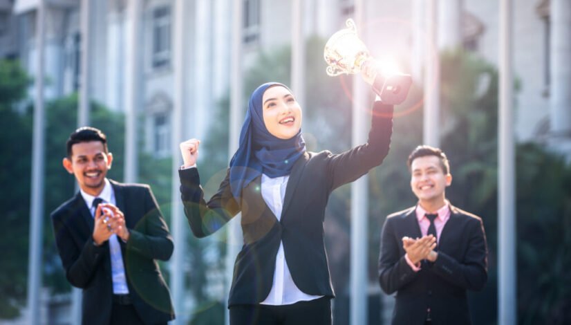 Successful Muslim business woman with arms up holding a trophy a